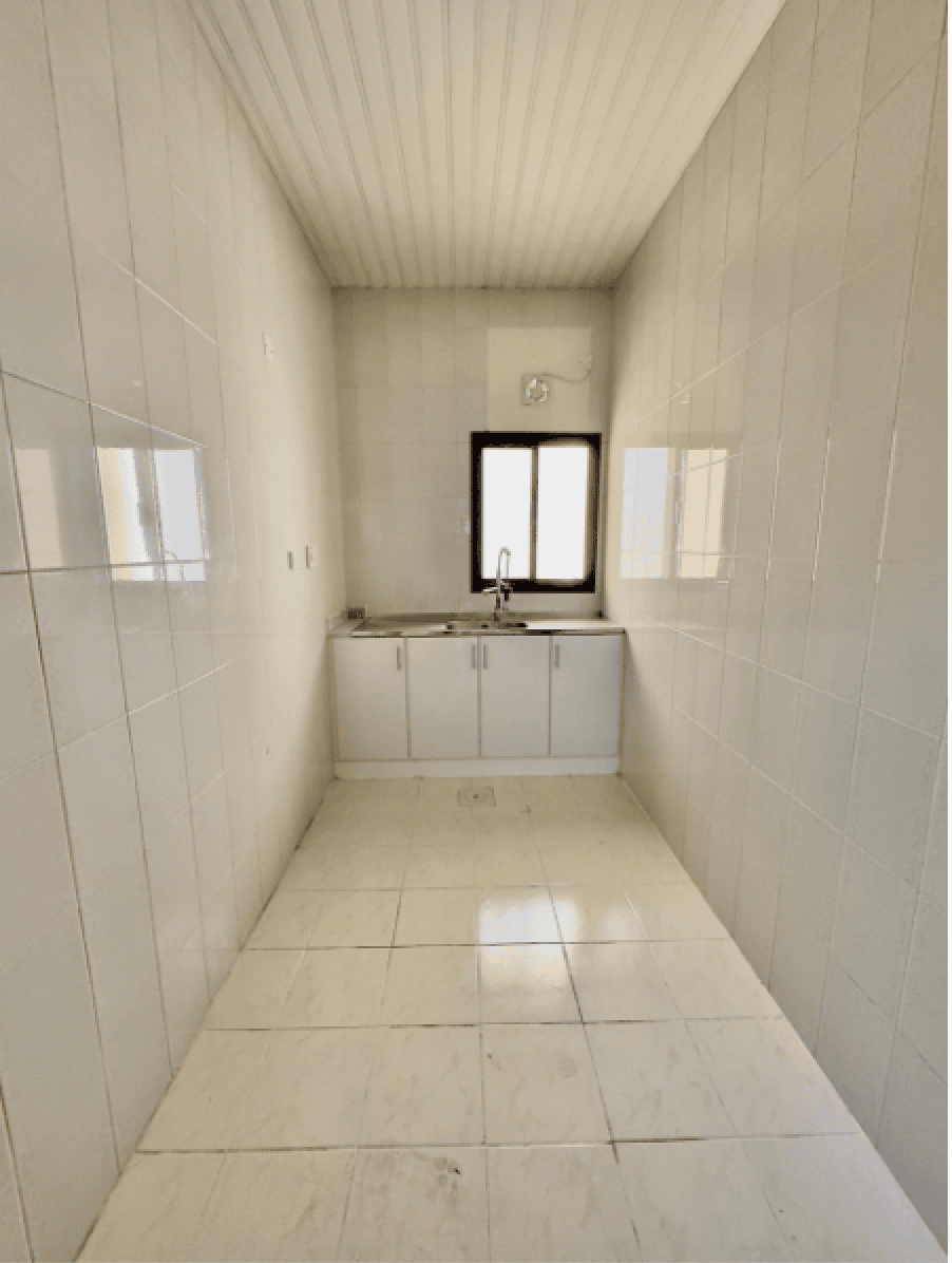 Narrow kitchen with white tiled walls and floor, featuring a single window and a small sink with cabinets underneath.